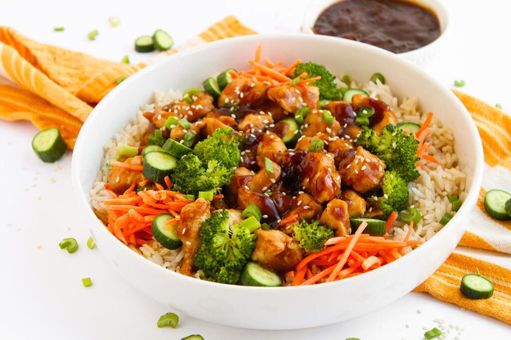 Front focus. A white bowl filled with Teriyaki chicken, veggies, and brown rice.