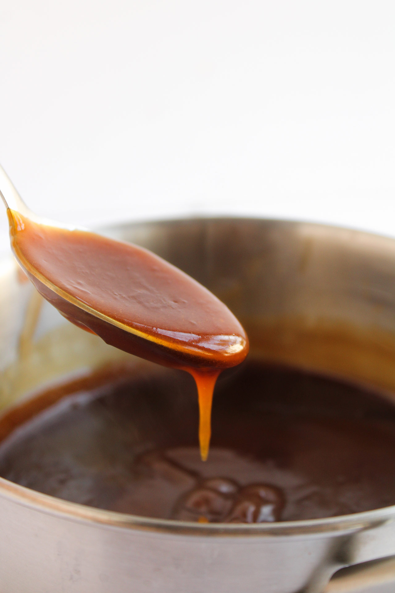 A spoon lifts out a bit of thickened teriyaki sauce from a pot.