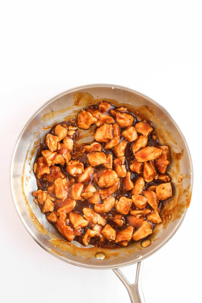 Chicken chunks in a skillet tossed with teriyaki sauce.