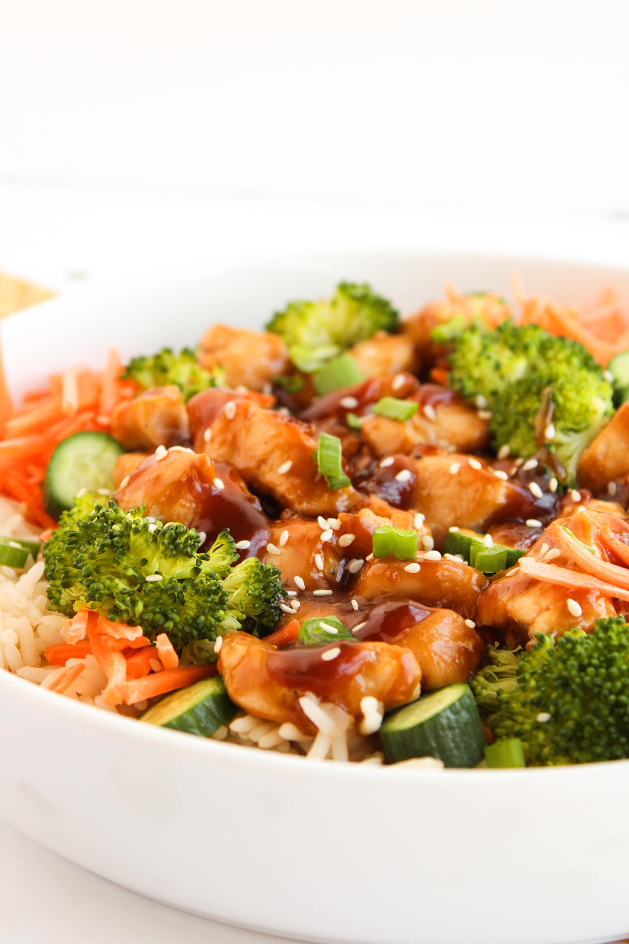 Front focus. A white bowl filed with ingredients that make up a Teriyaki chicken bowl.