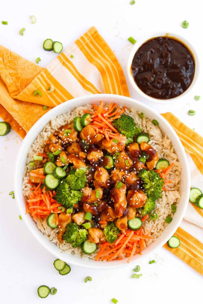 Overhead focus. A Teriyaki chicken bowl sitting on an orange, striped towel.