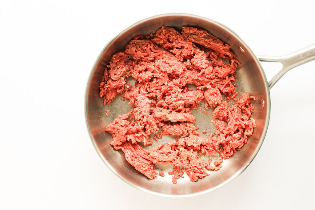 Raw, ground beef cooking in a skillet.
