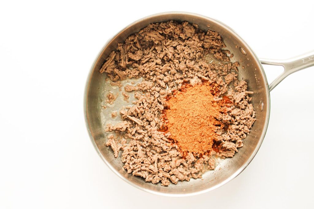 Taco seasoning added to cooked ground beef in a skillet.