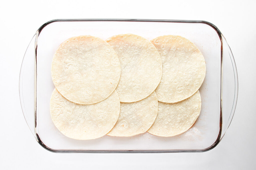 Corn tortillas lining the bottom of a glass casserole dish.