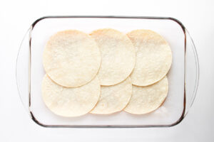 Corn tortillas lining the bottom of a glass casserole dish.